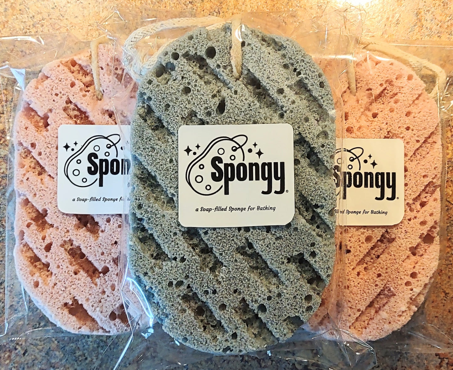 Three sponges in packaging with 'Spongy' branding on a wooden surface.
